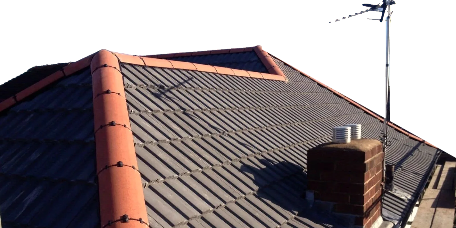 A newly re-roofed West Midlands hipped roof: grey concrete tiles, red dry-fix ridge and hip tiles, and a brick chimney